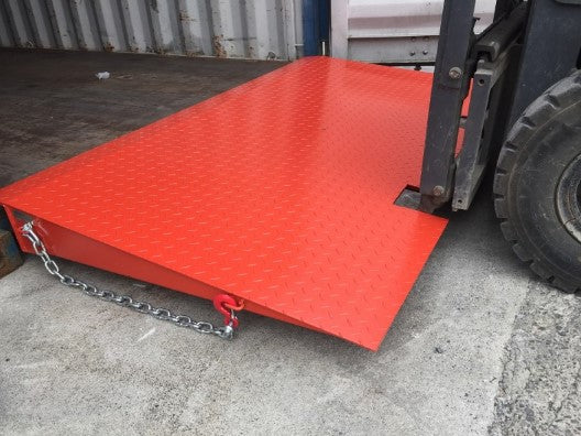 Heavy-duty red steel container ramp with safety chain in use by a forklift entering a shipping container.