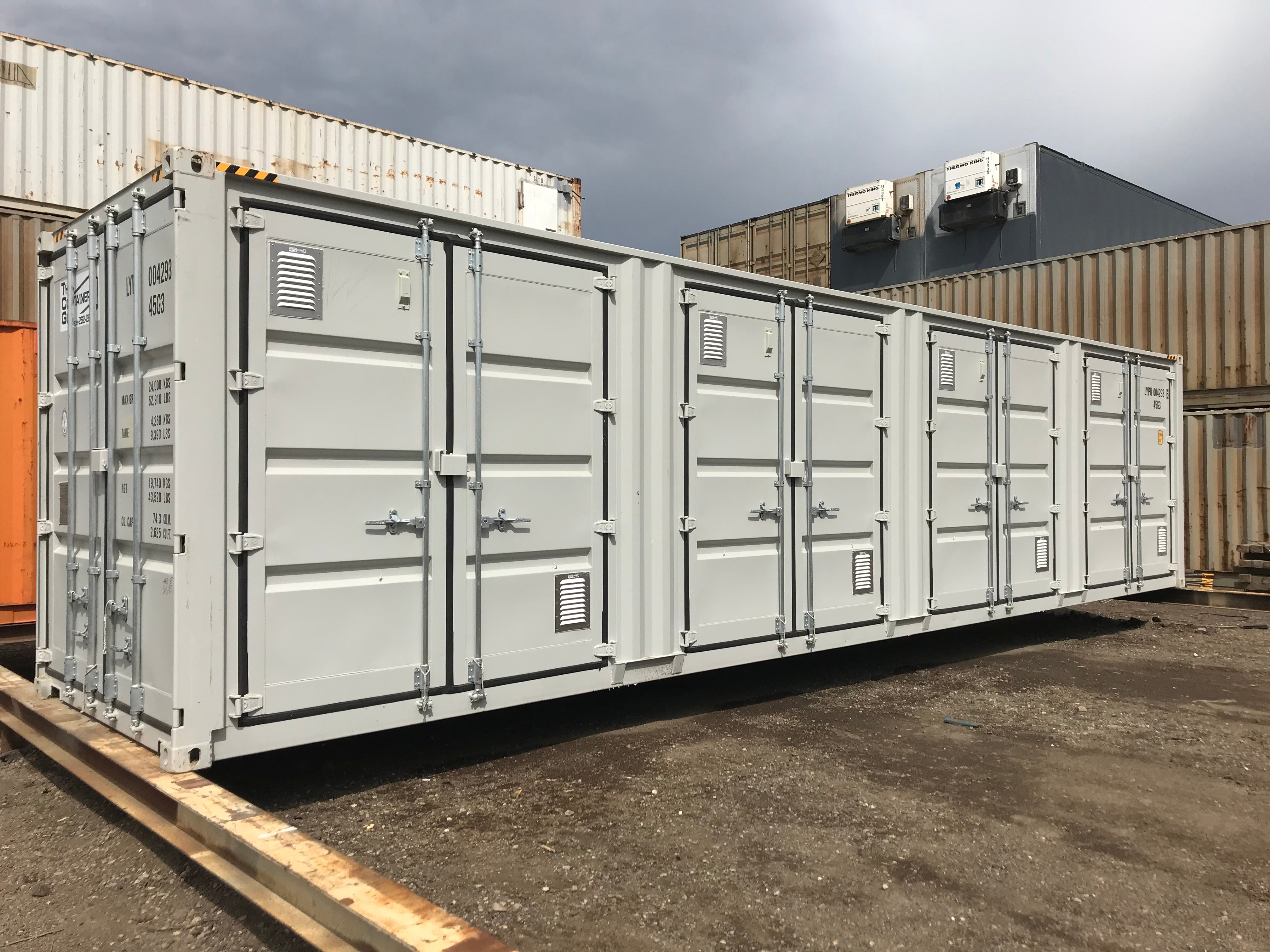 Multiple white shipping containers with Big Air 45 Louvered Gable Vents installed on the doors and side panels for ventilation, positioned in a container yard under a cloudy sky.