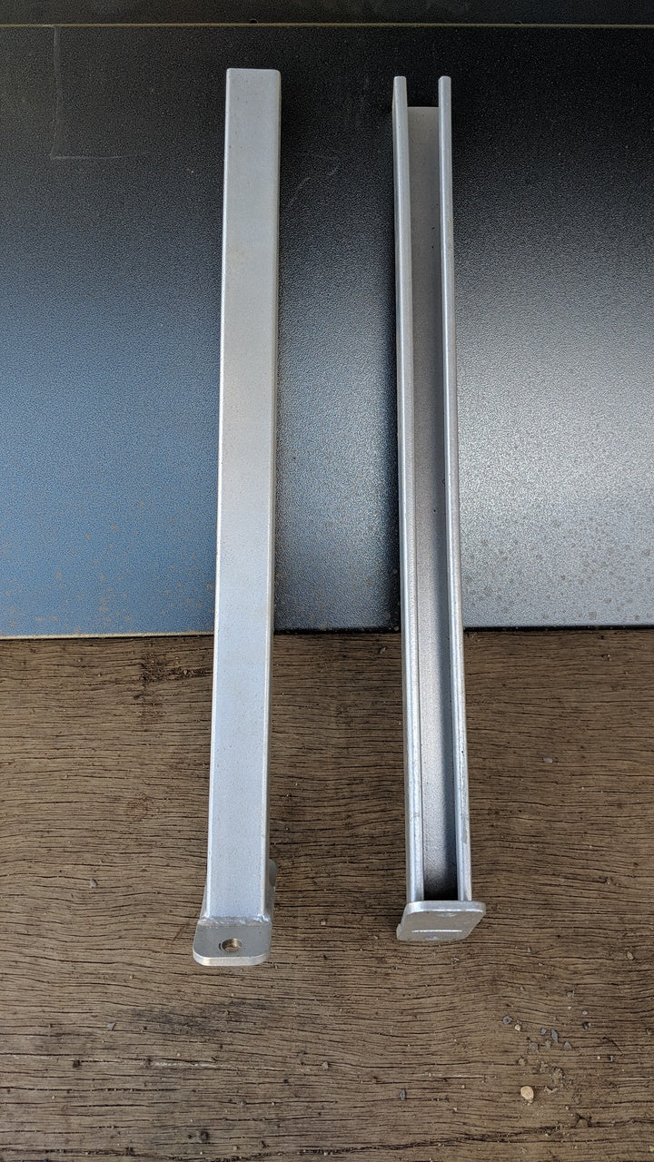 Top-down view of two galvanized steel CSM Pipe Rack arms placed side by side on a wood and metal surface, designed for adjustable pipe storage in shipping containers.