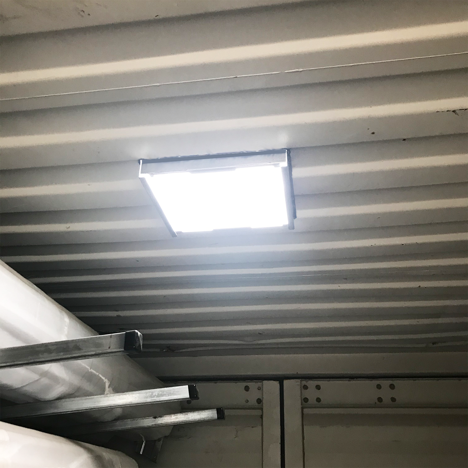Interior view of a shipping container with a mounted Big Air Sky Light Roof Vent installed on the ceiling, providing bright natural daylight through the corrugated steel roof